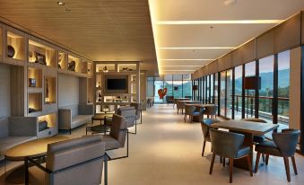 a modern , well - lit hotel lobby with various seating options and a large window offering a view of the mountains at Royal Tulip Golf Resort Gunung Geulis