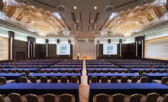 a large conference room with rows of chairs and tables , a chandelier , and screens on the walls at Hotel Metropolitan Akita