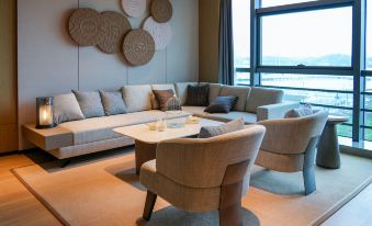 A spacious living room with large windows features comfortable couches and chairs arranged around a central table at Shantou Marriott Hotel