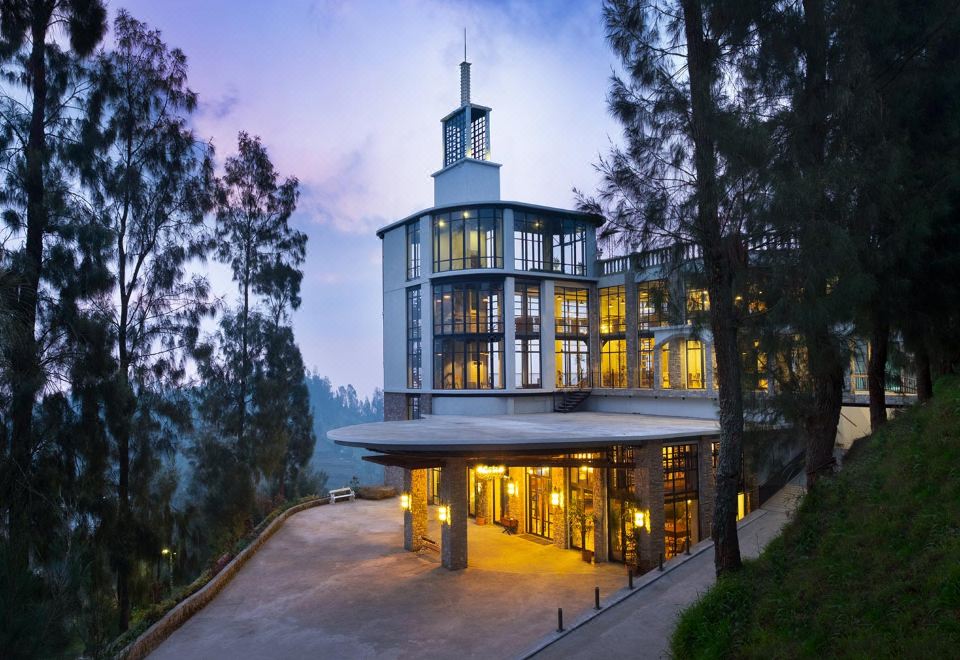 a modern building with a large glass window and a spire on the roof is surrounded by trees at Plataran Bromo