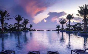 a beautiful sunset over a large body of water , with palm trees in the foreground at Movenpick Resort Cam Ranh
