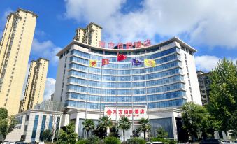 a large building with a red and white sign on top , surrounded by tall buildings and cars at Gushi Oriental Earl Hotel (Yucheng Avenue Genqin Culture Park)