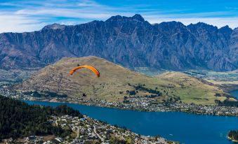 a person is flying a paraglider over a mountainous landscape with a city in the background at Oaks Queenstown Shores Resort