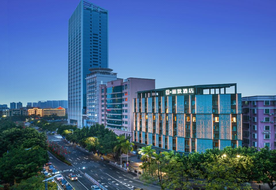 The city features tall buildings and a street running through the middle, with an office building on one side and a hotel on the other at Mehood Lestie Hotel (Maoming High-speed Railway Station)