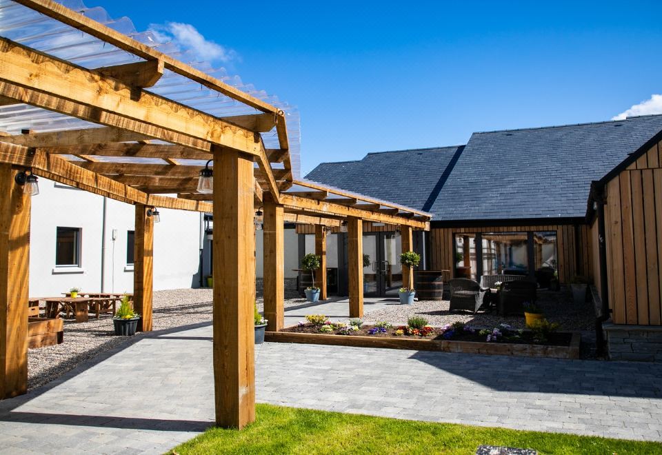 a wooden pergola in front of a house , surrounded by a grassy area and a pool at Hotel Doolin
