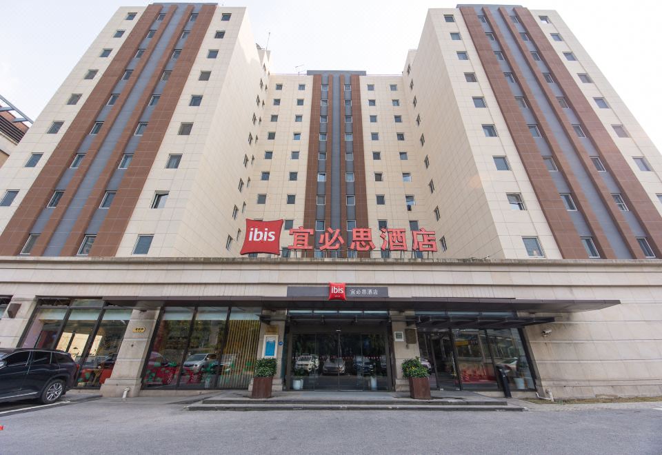 The front entrance of a hotel in an urban setting features large glass and steel doors at Ibis Hotel (Shanghai New International Expo Center Lianyang Branch)