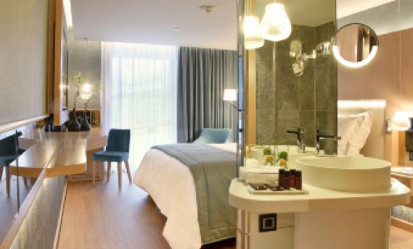 a modern bedroom with a large bed , white desk , and a mirror in the bathroom at Maestral Resort & Casino