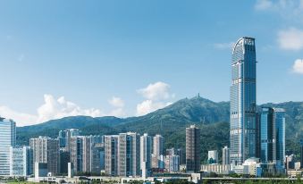 The cityscape features tall buildings and mountains in the background, viewed from across the water at Nina Hotel Tsuen Wan West