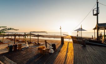 A wooden dock with chairs and tables is situated on the beach, providing a picturesque spot to enjoy the sunset at Aureum Palace Hotel & Resort, Ngapali