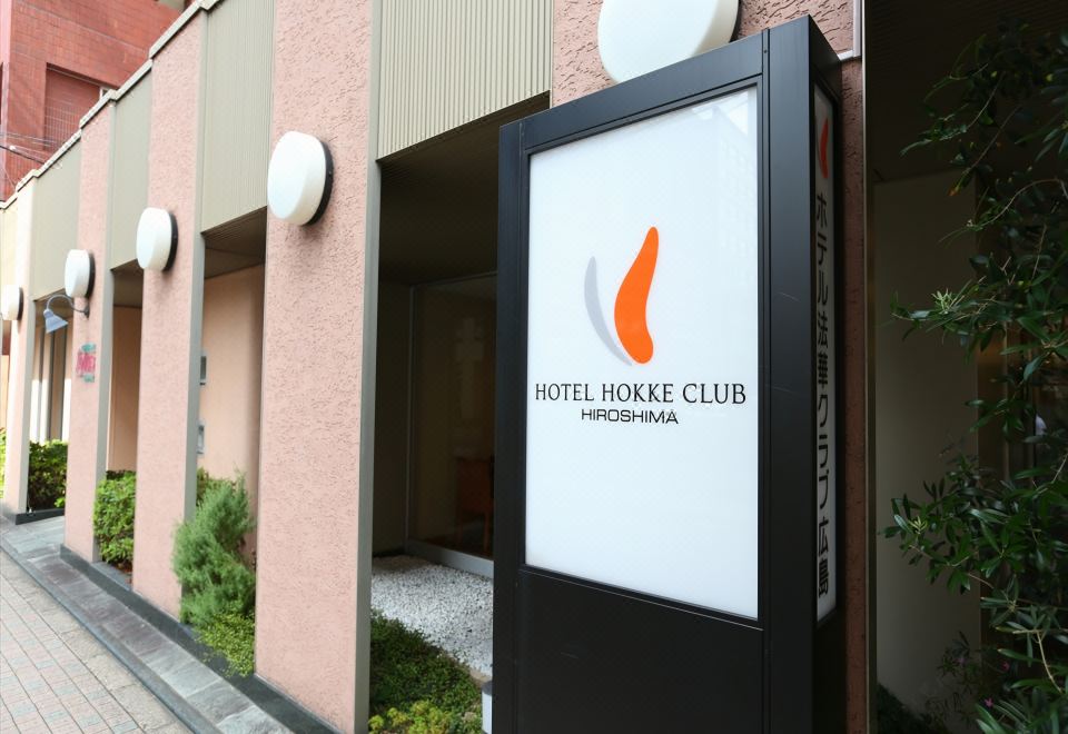 a sign for the hotel hoke club is displayed on a building with pink walls at Hotel Hokke Club Hiroshima