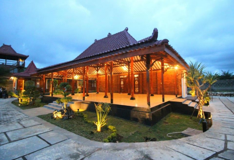 a wooden house surrounded by a lush garden , with a large pond in the center at The Royal Joglo