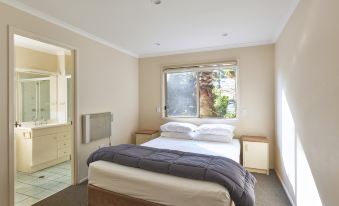 a bedroom with a large bed and white sheets , an air conditioner on the wall , and a window with curtains at Nrma Sydney Lakeside Holiday Park