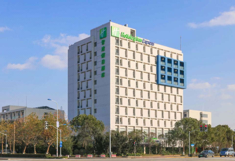 On a sunny day in an urban setting, there are clear front and side views of a large white building at Holiday Inn Express Shanghai Pudong Airport