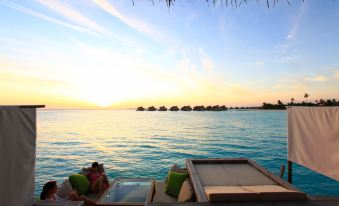 a serene beach scene at sunset , with a couple relaxing on lounge chairs overlooking the ocean at Six Senses Laamu
