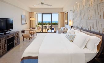 a large bed with white linens is in a room with a sliding glass door leading to an outdoor patio at The Romanos, a Luxury Collection Resort, Costa Navarino