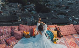 A woman is sitting on a roof with her legs up, while another person stands next to her at Lijiang YueJiaren · White Horse Luxury Homestay