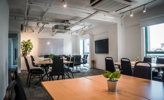 a modern office space with wooden tables , black chairs , and a large screen on the wall at Z Hotel