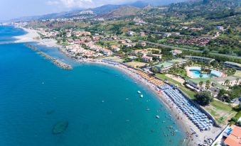 aerial view of a beach with numerous umbrellas and people enjoying the sunny day , surrounded by lush greenery and buildings at Hotel Poseidon