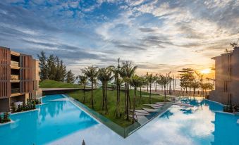 a large , modern swimming pool with palm trees and lounge chairs is surrounded by a serene ocean view at La Vela Khao Lak