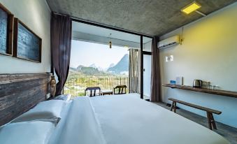 The bedroom offers expansive views of the city's mountains through its large windows and balcony at Yangshuo Sudder Street Guesthouse