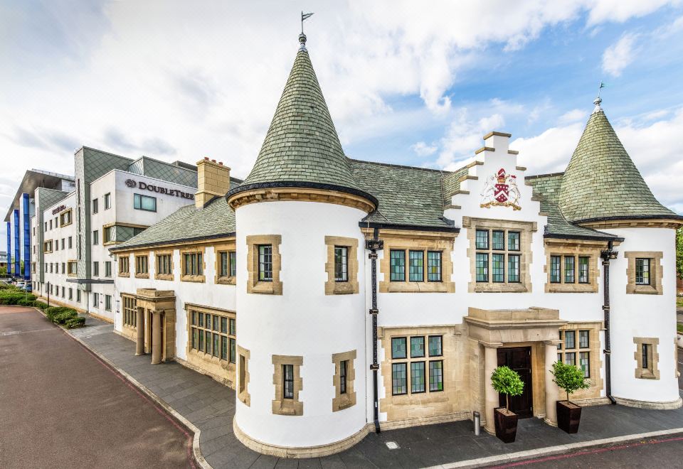 a large white building with a tower and green trim is surrounded by a large tree at DoubleTree by Hilton London Heathrow Airport