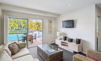 a living room with a large flat - screen tv mounted on the wall , a couch , and a dining table at Oaks Port Stephens Pacific Blue Resort