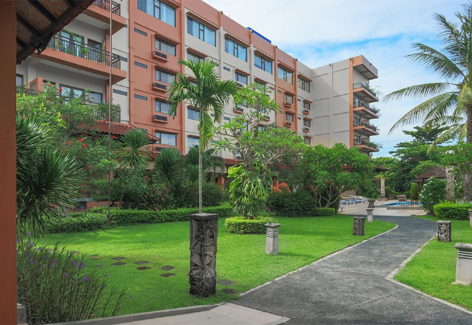 a green lawn with a tall palm tree and bushes in front of an apartment building at The Jayakarta Suites Komodo Flores