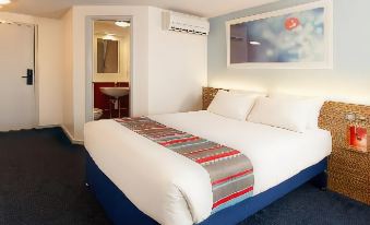a bed with a colorful blanket is in a room with a blue carpet and an open door at Travelodge Porthmadog