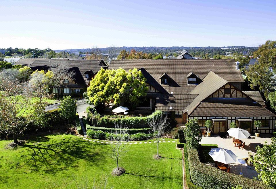 a large house surrounded by green grass and trees , with a pool in the background at Peppers the Hills Lodge