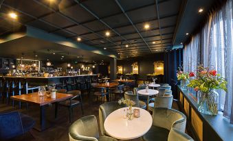 a modern restaurant with tables and chairs , a bar area , and a large window at Van der Valk Volendam