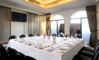 a large , round table with white tablecloth is set for a formal dinner in a room with multiple chairs and windows at Gambaro Hotel Brisbane