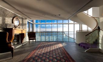 a spacious living room with a large flat - screen tv mounted on the wall , surrounded by windows that offer a view of the ocean at Cliff House Hotel