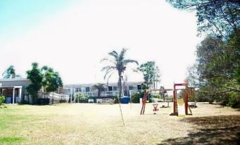 a sunny day with trees , grass , and a playground in front of a large building at Top of the Lake Holiday Units