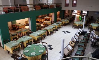 a large dining room with multiple tables and chairs , all set for a meal , is decorated with green tablecloths and white plates at Hotel Presidente