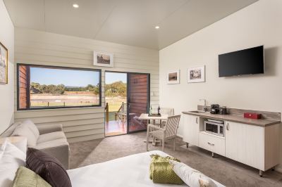 a small , modern hotel room with a bed , couch , dining table , and sliding glass doors leading to a patio at The Swan Valley Retreat