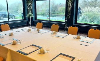 a large conference table with white tablecloths and orange chairs is set up in a room with large windows at Shillingford Bridge Hotel