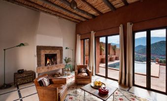 a living room with a fireplace , couches , and a coffee table is shown with a view of the mountains at Kasbah Bab Ourika