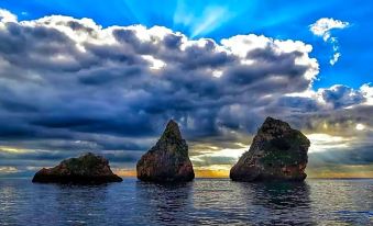 a picturesque sunset over the ocean , with three large rock formations jutting out of the water and a cloudy sky overhead at Moo