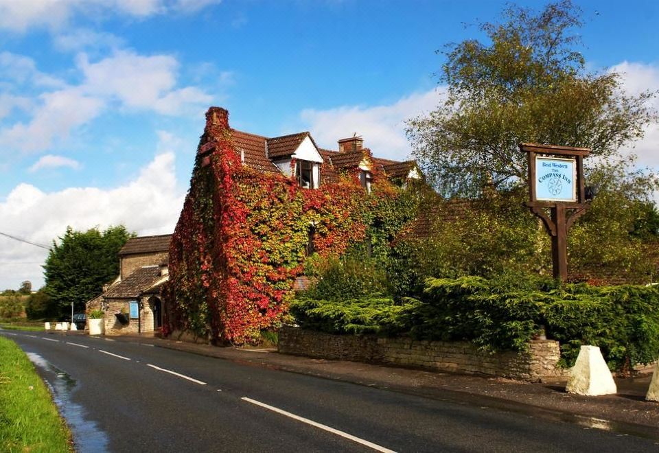 a brick building with a large red ivy growing on it , surrounded by a grassy area and trees at Best Western the Compass Inn