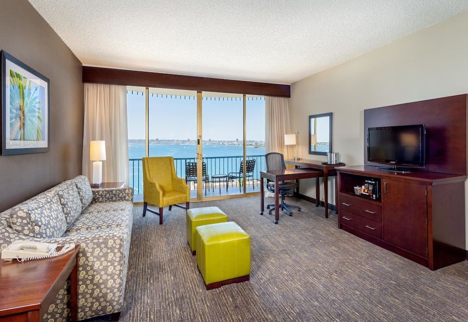 a hotel room with a couch , chairs , and a tv near a balcony overlooking the ocean at Wyndham San Diego Bayside