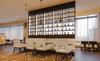 a restaurant with white chairs and tables , a bar counter , and shelves filled with various items at Hilton Albany