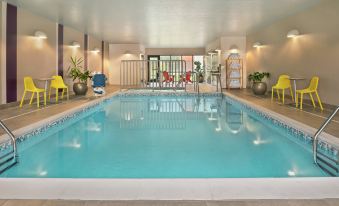 a large swimming pool with a white border and yellow chairs around it , surrounded by lounge chairs and potted plants at Home2 Suites by Hilton Marysville