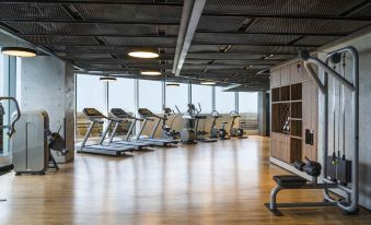 a large , well - lit gym with multiple treadmills and exercise equipment lined up in the center at Swissôtel Jakarta Pik Avenue