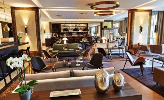 a spacious , well - lit room with a bar area and several chairs and couches arranged around it at Steigenberger Hotel Koln