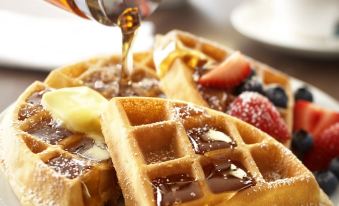 a plate of waffles topped with strawberries and blueberries , accompanied by a bottle of syrup at Country Inn & Suites by Radisson, Harrisburg Northeast - Hershey