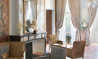 a luxurious living room with a fireplace , two chairs , and a statue on the wall at Chateau de Fonscolombe