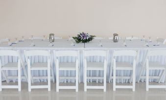 a long white dining table with chairs arranged around it , and a vase of flowers placed on the table at Travellers Beach Resort