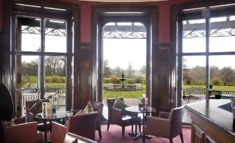 a large dining room with several chairs and tables , and a view of the outdoors through two large windows at Rookery Hall Hotel & Spa