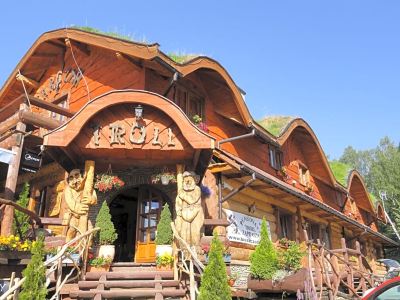 "a large wooden building with a sign that reads "" krause "" and two statues on the front" at Troll