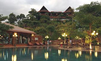 a large swimming pool surrounded by trees , with several lounge chairs and umbrellas placed around the pool area at Phu Pha Nam Resort